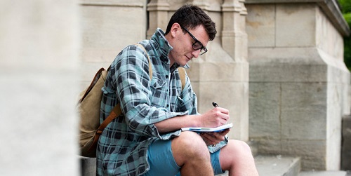 Student sitting on the steps of a building writing in a note pad